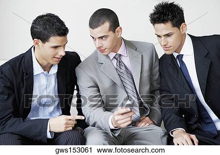 Close-up of three businessmen sitting and looking at a mobile phone View Large Photo Image Stock Image - Close-up of three businessmen sitting and looking at a mobile phone. Fotosearch