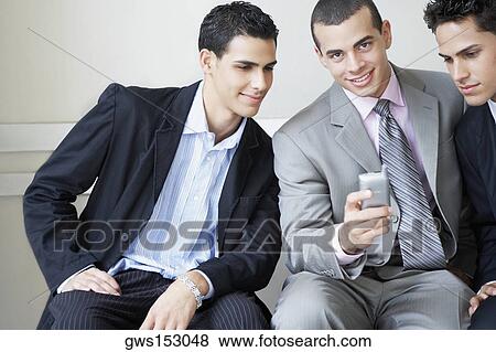 Portrait of a businessman holding a mobile phone with two businessmen looking at it View Large Photo Image Stock Photo - Portrait of a businessman holding a mobile phone with two businessmen looking at it. Fotosearch