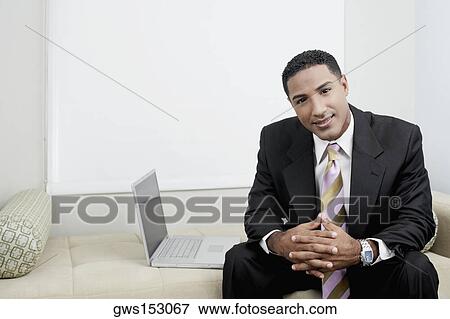 Portrait of a businessman sitting on a couch beside a laptop View Large Photo Image Stock Photo - Portrait of a businessman sitting on a couch beside a laptop. Fotosearch