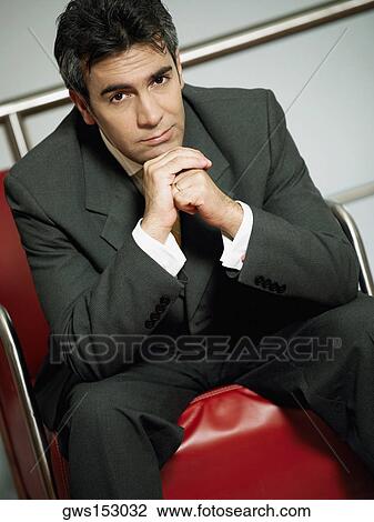 Stock Image - Portrait of a businessman sitting on an arm chair with his hand on his chin. Fotosearch