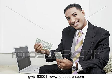Portrait of a businessman sitting beside a laptop and counting paper currency View Large Photo Image Stock Image - Portrait of a businessman sitting beside a laptop and counting paper currency. Fotosearch