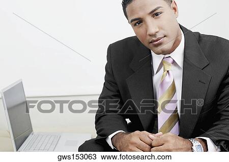 Stock Image - Portrait of a businessman sitting beside a laptop. Fotosearch