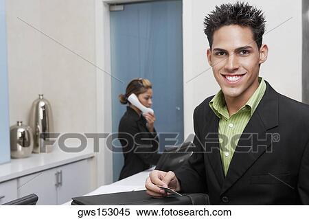 Portrait of a businessman standing at a hotel reception with a receptionist talking on the telephone behind him View Large Photo Image Stock Photography - Portrait of a businessman standing at a hotel reception with a receptionist talking on the telephone behind him. Fotosearch