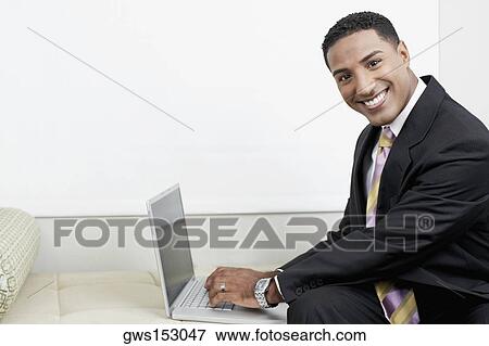 Stock Photo - Portrait of a businessman using a laptop and smiling. Fotosearch