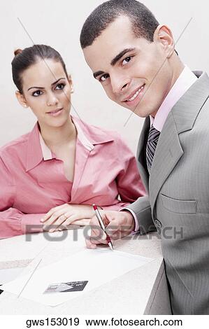 Portrait of a businessman writing on paper and a businesswoman standing beside him View Large Photo Image Stock Photo - Portrait of a businessman writing on paper and a businesswoman standing beside him. Fotosearch