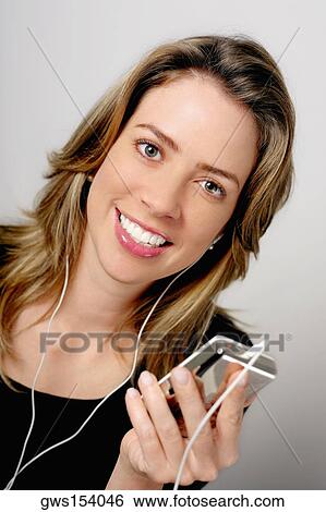 Portrait of a young woman holding an MP3 player and listening to music View Large Photo Image Stock Photograph - Portrait of a young woman holding an MP3 player and listening to music. Fotosearch