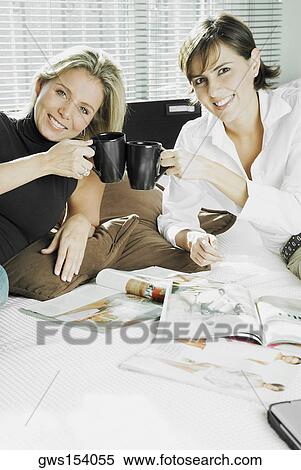 Stock Photography - Portrait of two mid adult women toasting cups of coffee and smiling. Fotosearch