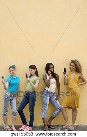 Stock Image - Four teenage girls using mobile phones and smiling. Fotosearch