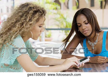 Two teenage girls sitting in a restaurant and looking at a mobile phone View Large Photo Image Stock Photo - Two teenage girls sitting in a restaurant and looking at a mobile phone. Fotosearch