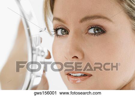 Stock Image - Portrait of a mid adult woman holding a pair of eyebrow tweezers. Fotosearch