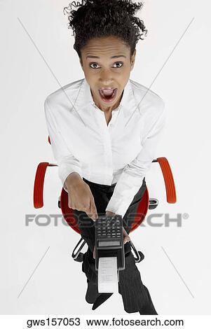 Stock Image - High angle view of a businesswoman operating an adding machine tape with her mouth open. Fotosearch