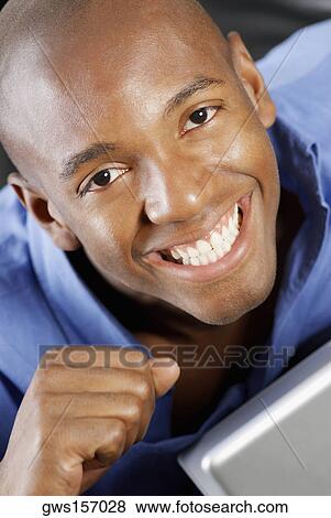 Stock Photo - Portrait of a young man smiling in front of a laptop. Fotosearch