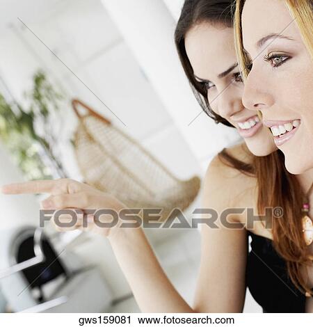 Stock Image - Close-up of two young women looking away and smiling. Fotosearch