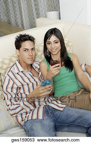 Stock Image - Portrait of a teenage girl and a young man sitting together on a couch holding drinks. Fotosearch