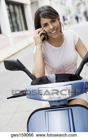 Portrait of a teenage girl riding on a motor scooter and talking on mobile phone View Large Photo Image Stock Photograph - Portrait of a teenage girl riding on a motor scooter and talking on mobile phone. Fotosearch