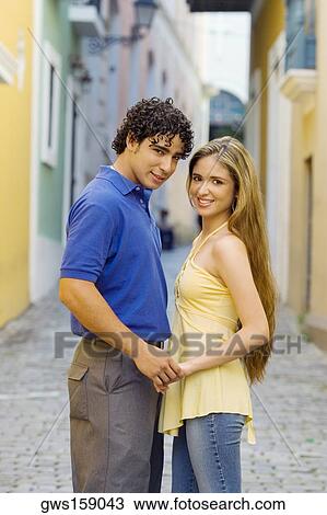 Stock Image - Portrait of a young man and a teenage girl standing on the street and holding hands. Fotosearch