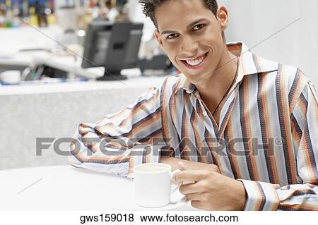 Stock Photo - Portrait of a young man holding a cup of coffee and smiling. Fotosearch