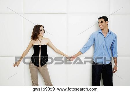 Young couple holding hands and standing beside a wall View Large Photo Image Stock Photo - Young couple holding hands and standing beside a wall. Fotosearch