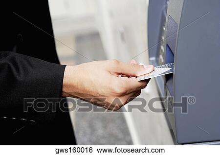 Stock Photograph - Close-up of a person's hand inserting a credit card into an ATM. Fotosearch