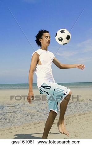 Stock Image - Teenage boy playing with a soccer ball on the beach. Fotosearch
