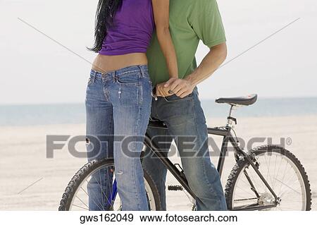 Stock Photo - Close-up of a young couple standing on the beach with a bicycle. Fotosearch