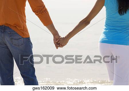 Mid section view of a young couple standing on the beach and holding hands View Large Photo Image Stock Photo - Mid section view of a young couple standing on the beach and holding hands. Fotosearch