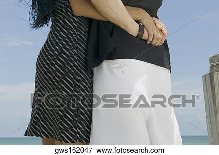 Stock Photo - Mid section view of a young couple standing on the beach. Fotosearch