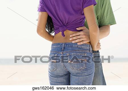 Stock Photograph - Mid section view of a young couple embracing each other on the beach. Fotosearch