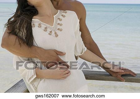 Mid section view of a young man embracing a young woman from behind View Large Photo Image Stock Photo - Mid section view of a young man embracing a young woman from behind. Fotosearch