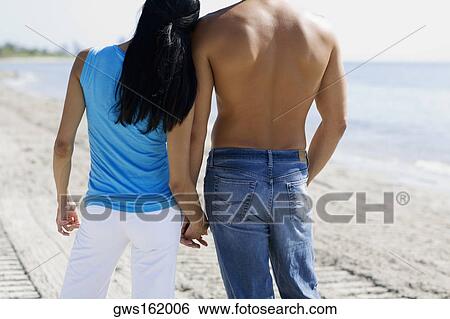 Rear view of a man and a woman holding hands on the beach View Large Photo Image Stock Photograph - Rear view of a man and a woman holding hands on the beach. Fotosearch