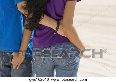 Rear view of a young couple standing on the beach with their arm around each other View Large Photo Image Stock Image - Rear view of a young couple standing on the beach with their arm around each other. Fotosearch
