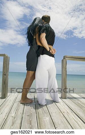 Rear view of a young couple standing on a pier View Large Photo Image Stock Image - Rear view of a young couple standing on a pier. Fotosearch
