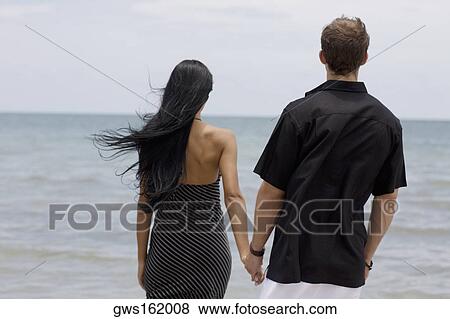 Rear view of a young couple standing on the beach View Large Photo Image Stock Photo - Rear view of a young couple standing on the beach. Fotosearch