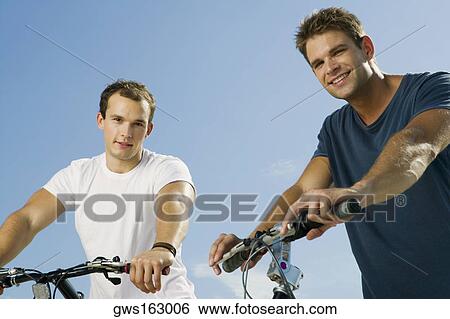 Stock Photograph - Portrait of two young men smiling and holding bicycles. Fotosearch