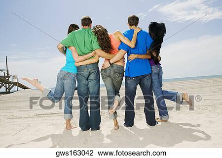 Stock Image - Rear view of five people standing on the beach. Fotosearch