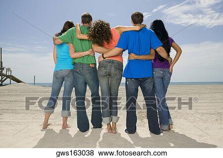 Rear view of five people standing on the beach View Large Photo Image Stock Photo - Rear view of five people standing on the beach. Fotosearch