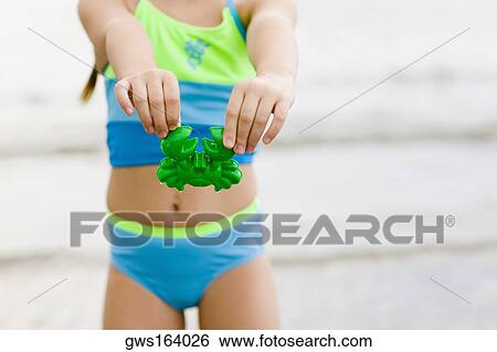 Stock Photograph - Mid section view of a girl standing on the beach and holding a toy. Fotosearch