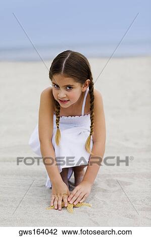 Stock Image - Portrait of a girl crouching on the beach. Fotosearch