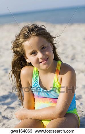 Stock Image - Portrait of a girl sitting on the beach and smiling. Fotosearch
