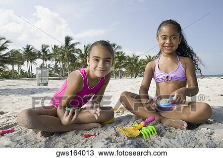 Portrait of two girls sitting on the beach and playing with sand View Large Photo Image Stock Image - Portrait of two girls sitting on the beach and playing with sand. Fotosearch