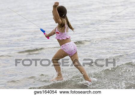 Side profile of a girl running on the beach and holding a sand pail View Large Photo Image Picture - Side profile of a girl running on the beach and holding a sand pail. Fotosearch