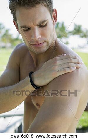 Close-up of a young man with his hand on his shoulder View Large Photo Image Stock Photo - Close-up of a young man with his hand on his shoulder. Fotosearch