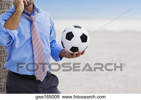 Mid section view of a man holding a soccer ball and talking on a mobile phone View Large Photo Image Stock Photo - Mid section view of a man holding a soccer ball and talking on a mobile phone. Fotosearch