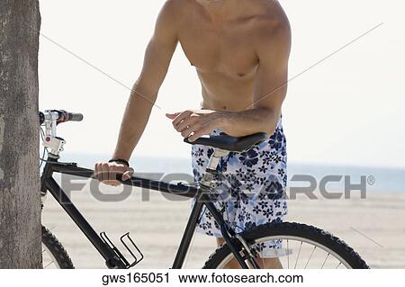 Mid section view of a man standing and holding a bicycle on the beach View Large Photo Image Stock Image - Mid section view of a man standing and holding a bicycle on the beach. Fotosearch
