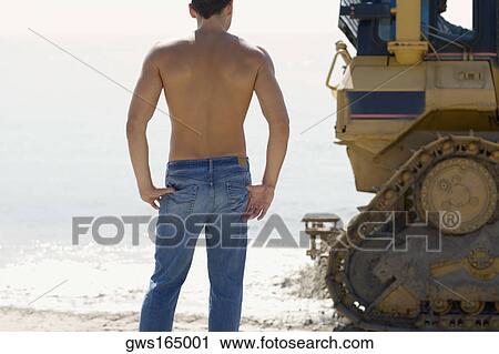 Rear view of a mid adult man standing behind an earth mover on the beach View Large Photo Image Stock Image - Rear view of a mid adult man standing behind an earth mover on the beach. Fotosearch
