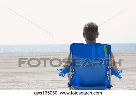 Rear view of a young man sitting on a lounge chair on the beach View Large Photo Image Stock Image - Rear view of a young man sitting on a lounge chair on the beach. Fotosearch