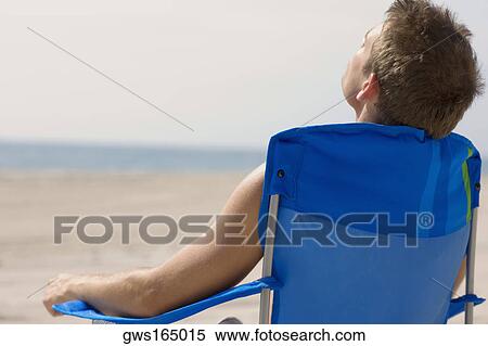 Rear view of a young man sitting on the beach View Large Photo Image Stock Photography - Rear view of a young man sitting on the beach. Fotosearch