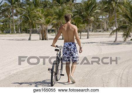 Rear view of a young man walking with a bicycle on the beach View Large Photo Image Stock Photography - Rear view of a young man walking with a bicycle on the beach. Fotosearch