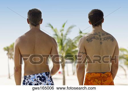 Stock Photograph - Rear view of two men standing on the beach. Fotosearch