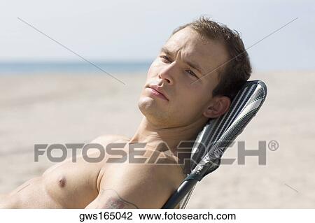 Stock Image - Side profile of a young man relaxing on the beach. Fotosearch